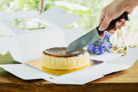 Woman's hand cutting basque burnt cheesecake with knife on wooden table. Stock Photos