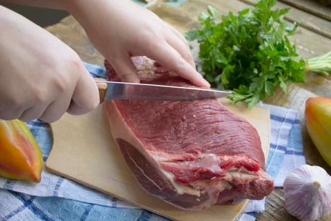 Womans hand cutting raw beef meat. close up Stock Photos