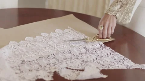 Woman's hand cutting with scissors a pattern of white lace fabric on a table Stock Footage 61738177