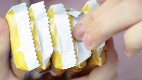 Woman's hand is cutting some chocolate bars or cookies wrapped in plastic pack 库存影片 181977588