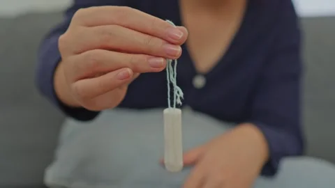 Woman's hand dangling clean white cotton tampon by its blue string Stock Footage 340576071