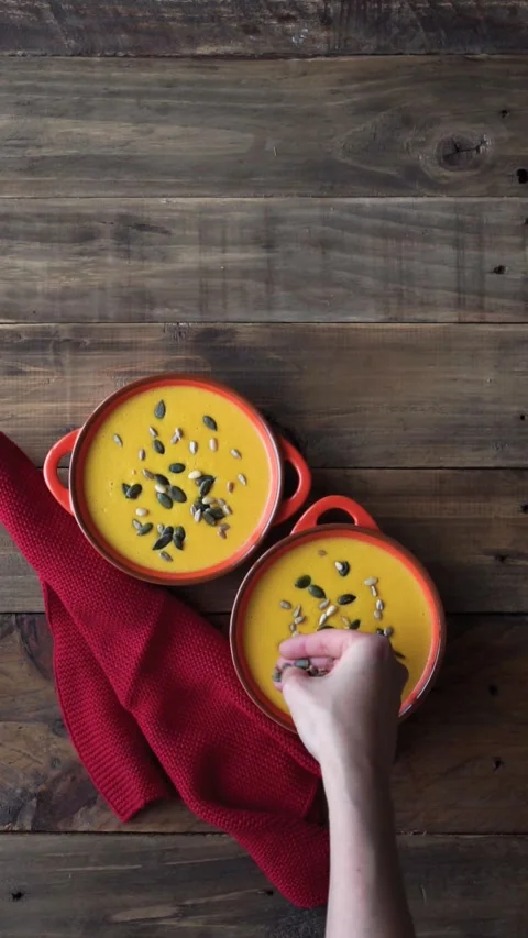 Woman's hand decorating two bowls of pumpkin cream with seeds. Food. Stock Footage 252139844