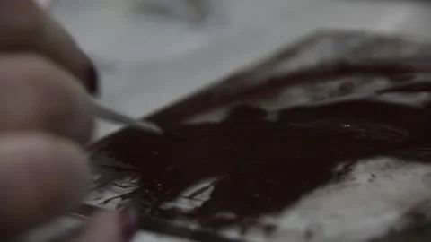 A woman's hand dips the brush into the dark brown paint on the palette. Video stock 130526244