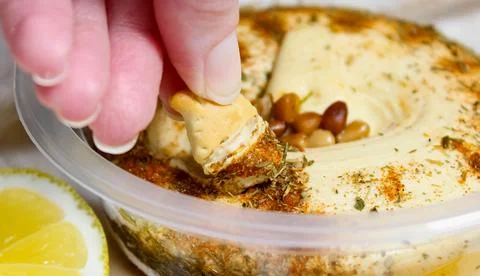 A woman's hand dips a cracker into a cup of hummus. Foto stock