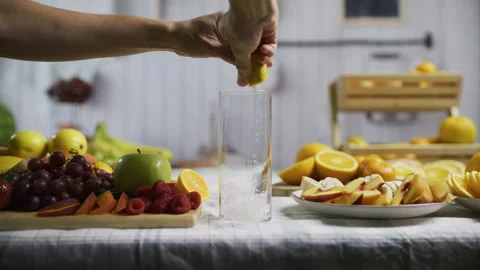 Woman's hand dropping ice, lemon and other juices into glass with surrounding Stock Footage 341256248