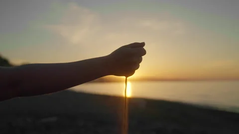 A woman's hand dropping sand at sunrise on the beach Stock Footage 200858747