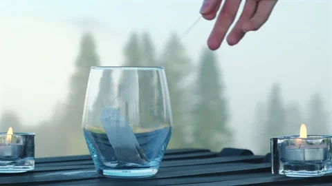 Woman's hand drops tea bag into glass cup. Process of making tea outdoors. Mug Video stock 254485278