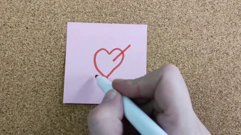 A woman's hand with a felt-tip pen drawing a heart on a pink sticker 库存影片 170332679