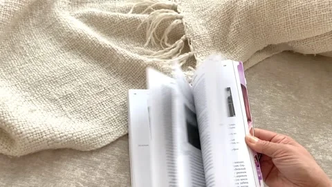 Woman's hand is flipping through book while sitting on sofa with plaid View from Stock Footage 267728611