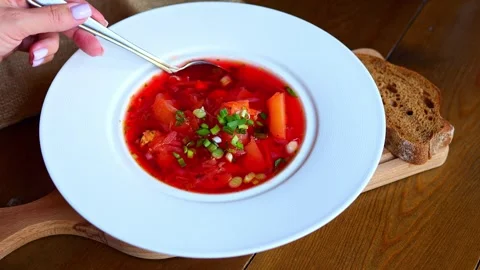 Womans hand gently stirs vibrant beetroot soup in bowl, creating mesmerizing Stock Footage 273204500