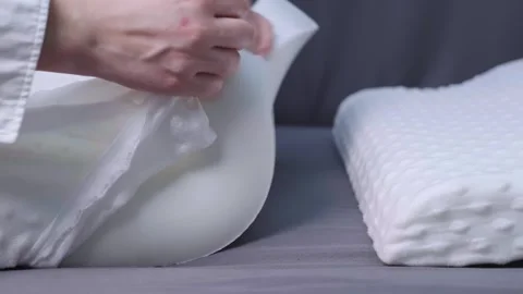 A woman's hand glides over a memory foam pillow on a gray bed, showcasing an ort Stock Footage 299722215