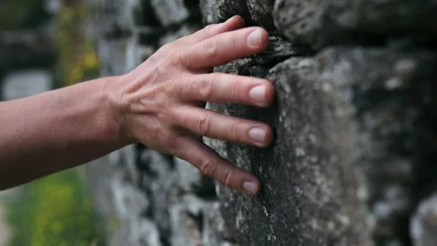 A woman's hand glides slowly along the textured surface of a stone wall, in a Video stock 243727067