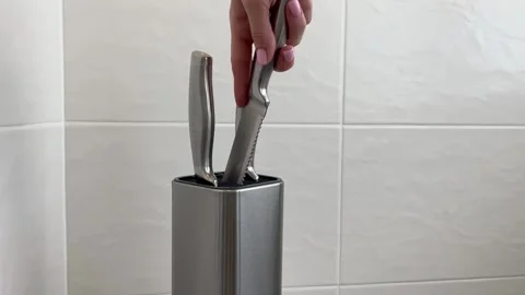 A woman's hand goes in turn to knives with a metal stand. Video stock 200606576