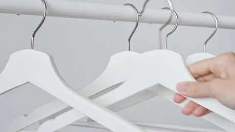 Woman's hand hangs white empty wooden clothes hanger on rack on white wall Stockbeeldmateriaal 193590412