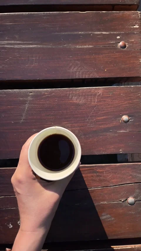 Woman's hand holding coffee over a wooden park bench Stock Footage 342977386
