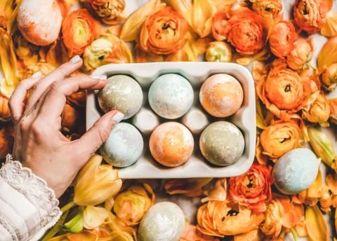 Womans hand holding dyed Easter egg over flowers, top view Stock Photos