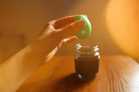 Woman's hand holding easter egg above paint jar Stock Photos