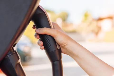 Woman's hand holding an electric vehicle or EV car socket in a charging stati Stock Photos