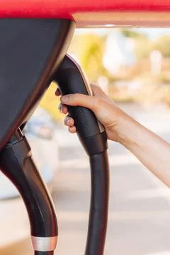 Woman's hand holding an EV or electric car socket in a charging station. Elec Stock Photos
