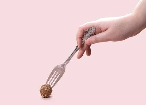 Woman's hand holding a fork to take chocolate ball. Pink background. Stock Photos
