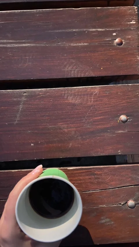 Woman's hand holding a green coffee cup over a wooden park bench Stock Footage 342977385
