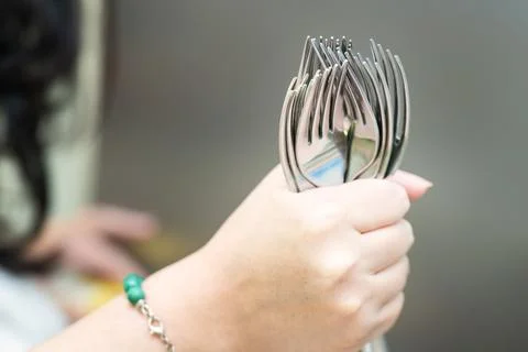 Woman's hand holding a large bundle of metal forks, showcasing dining essen.. Stock Photos