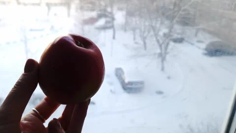 Womans Hand Holding Red Apple Against Snowy Winter Window Video stock 326312941