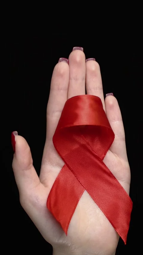 Woman's hand holding a red satin awareness ribbon on black background.  Stock Footage 345138754