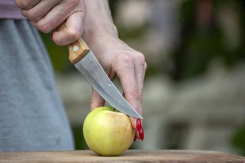 Woman's hand holding a sharp kitchen knife carefully cuts a fresh raw green.. Stock Photos