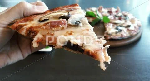 Woman's Hand Holding A Slice Of Mushroom And Bacon Pizza