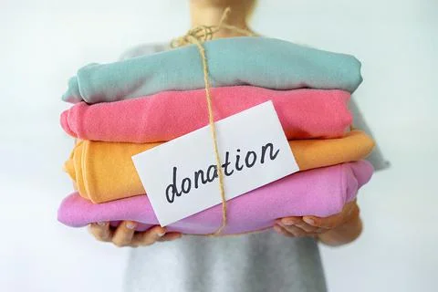 Woman's hand holding a stack of clothes. Clothes Donation, Renewable Concept Stock Photos