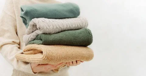 Woman's hand holding a stack of clothes. Clothes Donation, Renewable Concept Stock Photos