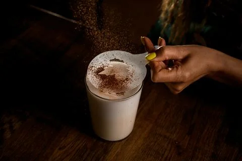 Woman's hand holding stencil with pattern over a glass of milk and pours cocoa Foto stock