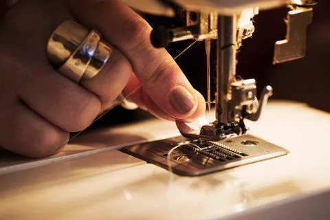 A woman's hand holding thread and threading a sewing machine needle. Stock Photos