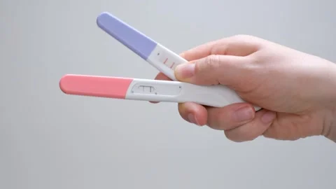 A womans hand holding two positive pregnancy tests on gray background. Stock Footage 324449487