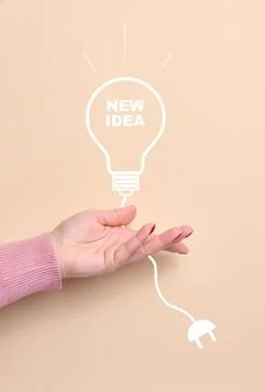 A woman's hand holds a drawn light bulb with the inscription New Idea and a.. Stock Photos