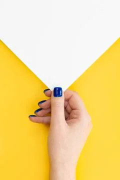 A woman's hand holds an empty sheet of paper on a yellow background, top view. Stock Photos
