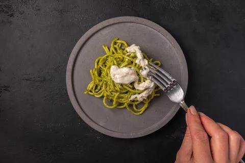 Woman's hand holds a fork with a paste with strachatella and pesto Stock Photos