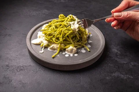 Woman's hand holds a fork with a paste with strachatella and pesto Stock Photos