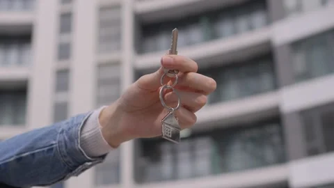 Woman's hand holds key keychain in form of house against background of building 스톡 동영상 237241271