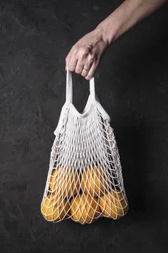A woman's hand holds a string bag with oranges on a dark textured background Stock Photos