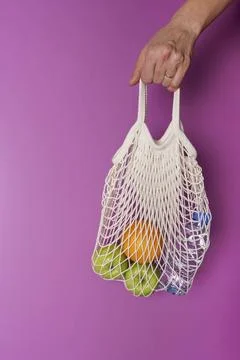 A woman's hand holds a string bag with oranges, apples and a bottle of water 库存照片