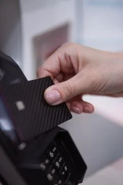 Woman's hand inserting a black carbon fiber credit card into a pos terminal.. Stock Photos
