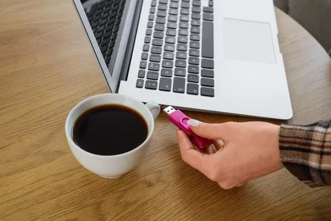 Womans hand inserting pink USB flash drive into laptop port on wooden table w Stock Photos