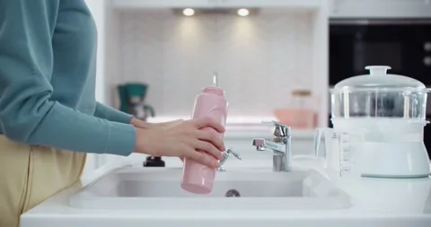 Woman’s hand in the kitchen draw filtered water into a sports pink bottle. Vidéo 230644552