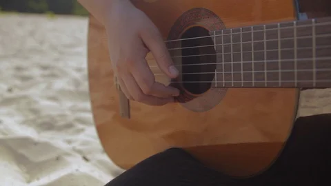 Woman's hand knocks and playing guitar on sandy beach, sunny day, close up Stock Footage 127717363