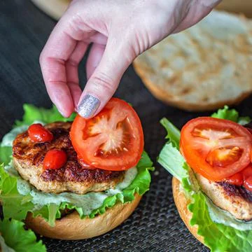 A woman's hand lays down a slice of tomato on a delicious homemade burger Foto stock
