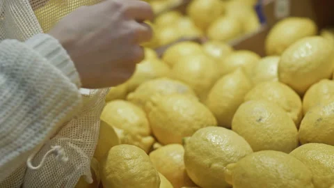 Woman's hand lays lemons in string bag. Close-up. Shop with this environmentally Stock Footage 146450343