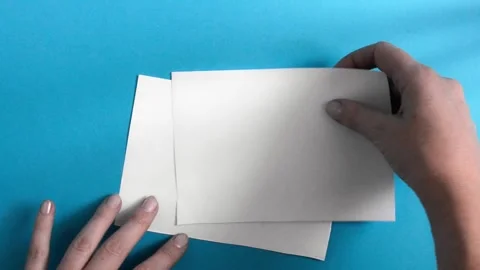 A woman's hand lays out two blank white sheets on a blue background Stock Footage 150948861
