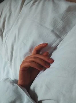 A woman's hand is lying on the pillows covered with a blanket Stock Photos